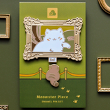 Meowster Piece enamel pin set packaging on a green background with decorative frames.