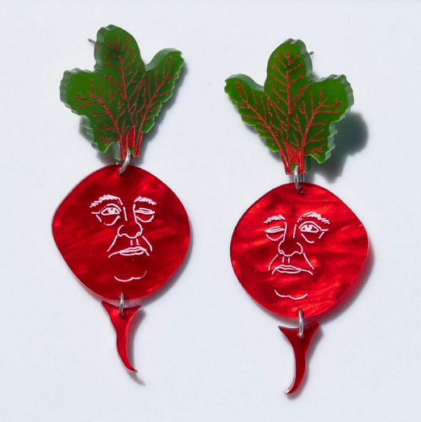Two decorative beet earrings on a white plate with a red and white checkered tablecloth background.
