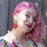 Woman with pink hair wearing a colorful floral dress against a wooden fence.