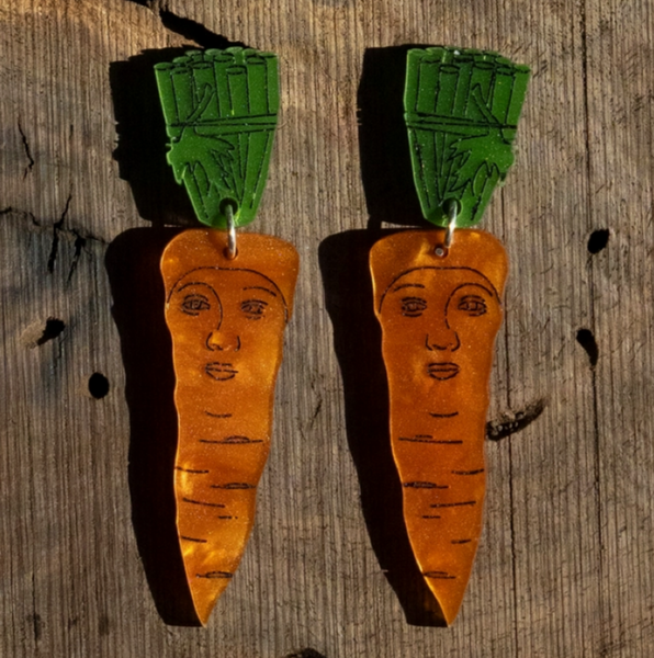 Carrot-shaped earrings with face details on a wooden background