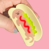 Hand holding a cute hot dog-shaped object with a pink background