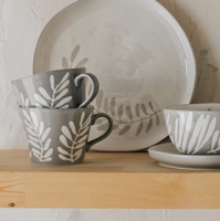 Ceramic dishes with leaf patterns on a wooden shelf against a light-colored wall.