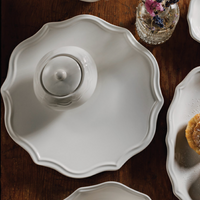 White ceramic dishes on a wooden table with a small vase of flowers.