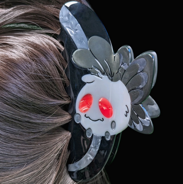 Hair clip with cartoonish design of a face with red cheeks and transparent wings on a person's hair.