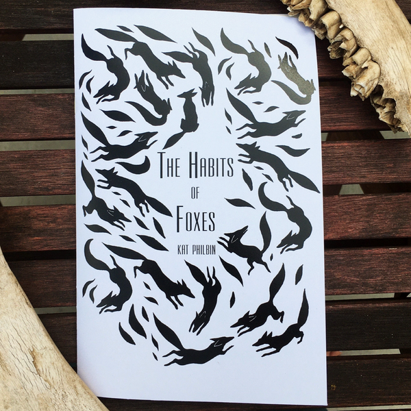 Book cover of 'The Habits of Foxes' with black fox illustrations on a white background, displayed on a wooden surface.