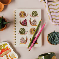 Tabletop scene with stationery items including a notebook, mugs, and decorative plants on a light surface.