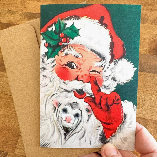 Vintage-style Christmas card with Santa Claus and a mouse, held by a hand on a wooden surface.