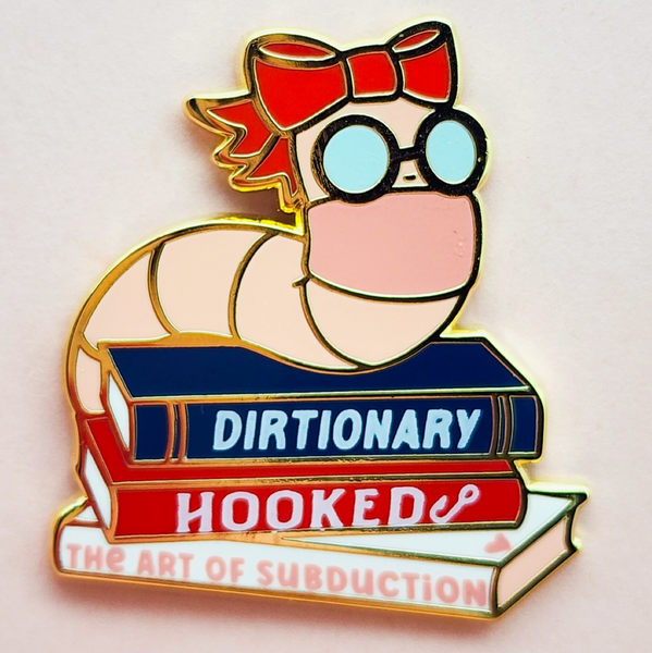 Pin with cartoon character on a dictionary book titled 'Hooked: The Art of Subduction' on a light gray background.
