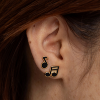 Close-up of an ear wearing a black music note earring with hair partially covering the frame.
