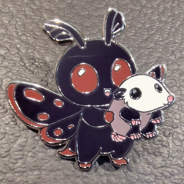 Enamel pin of a stylized creature with butterfly wings on a textured gray background