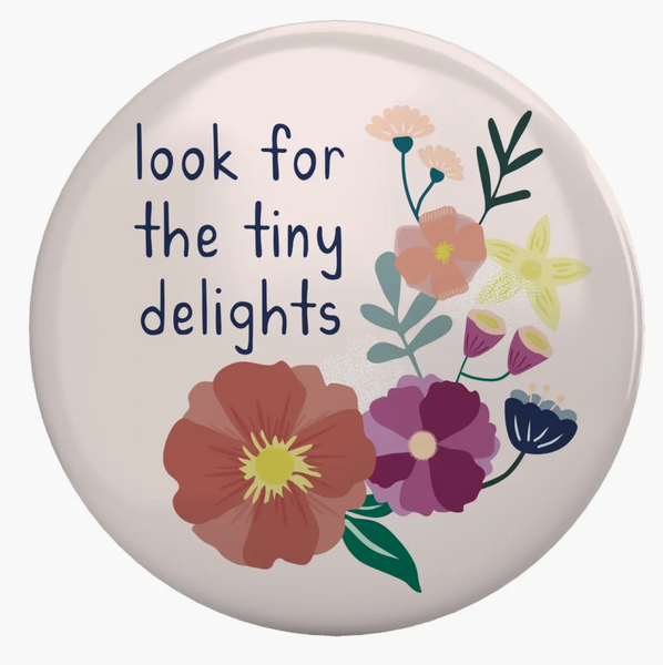 Decorative button with floral design and text 'look for the tiny delights' on a white background.
