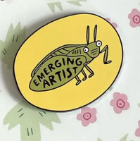 Pin with 'Emerging Artist' design on a branded card with floral patterns