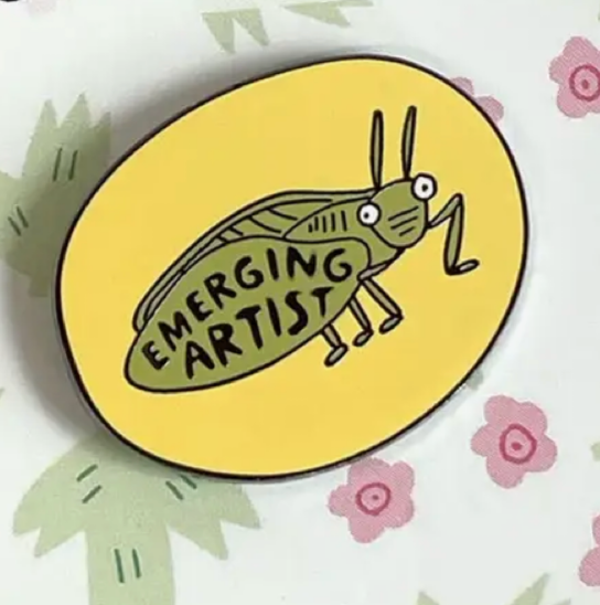 Pin with 'Emerging Artist' design on a branded card with floral patterns