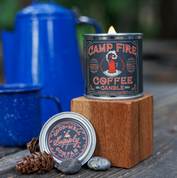 Campfire coffee candle with blue enamel mug and pinecones on a wooden surface