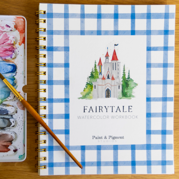 Fairytale watercolor workbook with a castle design on a blue and white checkered cover, accompanied by a paintbrush and watercolor palette.