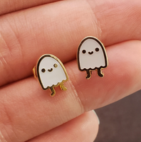 Two small ghost-shaped earrings held between fingers against a dark background